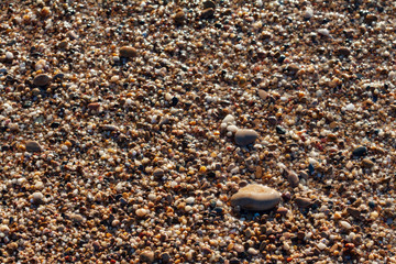 sea pebbles colored granite on the beach background stones. The shore of the beach with sand and pebbles washed by the waves of the sea.