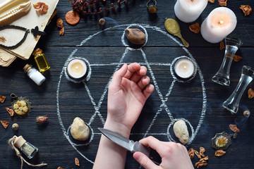 Womens hands and knife on pentagram circle with candles, stones, love potion and old books on witch...