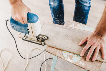 Top view on hands of a caucasian man with a jigsaw - housework sawing a board