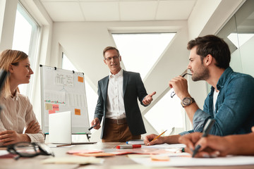 Brainstorming. Mature businessman in formal wear standing near whiteboard and explaining something...