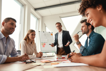 Working together. Mature businessman in formal wear standing near whiteboard and explaining something to his colleagues