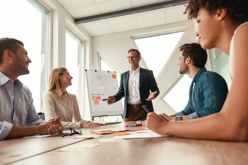 Best team Mature businessman in formal wear standing near whiteboard and smiling while working together with young colleagues in the modern office