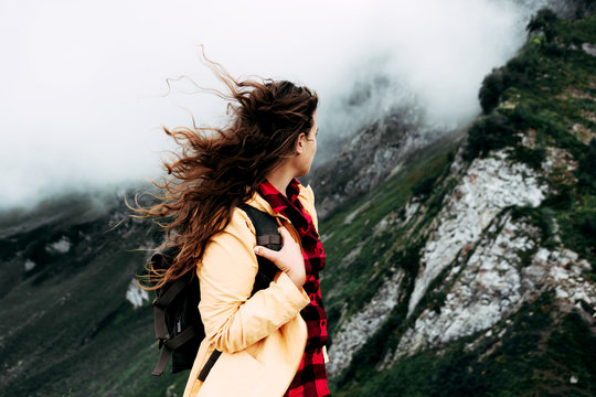 A Girl With Long Curly Hair Developing In The Wind Turned Away From The Camera And Looks At The Mountain Landscape.