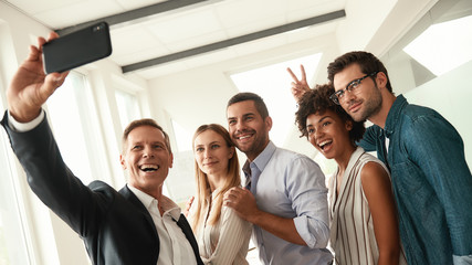 Happy moments. Group of smiling colleagues taking selfie and gesturing while standing in the modern...