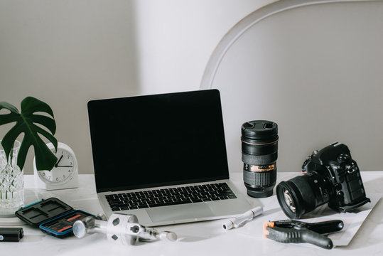 Still life working from home desk with professional photographic equipment, camera, lens, computer monitor, electronics indoors.