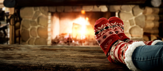 Woman legs with christmas socks and fireplace  - obrazy, fototapety, plakaty