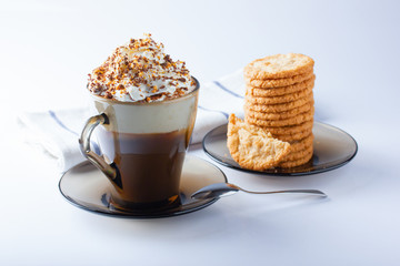 Coffee, cappuccino with whipped cream sprinkled with chocolate chips, ground nuts, cinnamon. Oatmeal cookies, stacked on a plate. Napkin, dessert spoon. The photo.