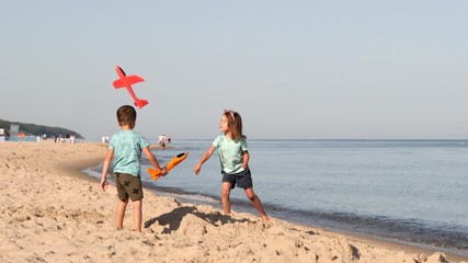 Little boy and girl play on baltic sea sand beach launching red toy plane having fun