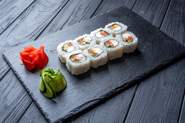 Set of sushi rolls with cream cheese, rice and salmon on a black board decorated with ginger and wassabi on a dark wooden background. Japanese cuisine. Food photo background