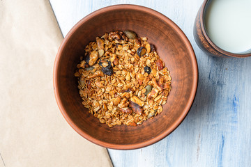 Granola in a brown clay bowl with a glass of milk. Tasty and healthy breakfast. Blue wood background. Top view. Flat lay food