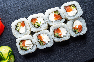 Set of sushi rolls with cream cheese, rice and salmon on a black board decorated with ginger and wassabi on a dark wooden background. Japanese cuisine. Food photo background