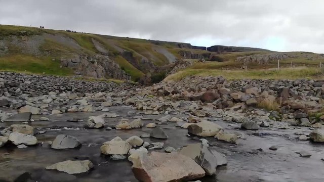Hengafoss' stream in Iceland. The drone follows it up stream. The background is typical of Icelandic beauty. Thick white clouds can be seen in the sky along with the waterfall.
