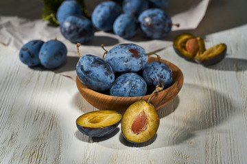 Raw plums in a plate on a white wooden background