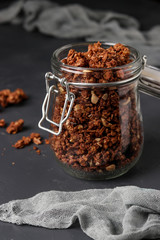 Granola crispy muesli with natural honey, chocolate and nuts in a glass jar against a dark background, healthy food, vertical orientation