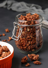 Granola crispy muesli with natural honey, chocolate and nuts in a glass jar against a dark background, healthy food, vertical orientation