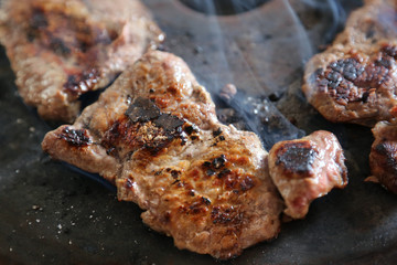 Simple cooking.The meat is fried on a black primitive black roasting pan and slightly charred. Hot steam flows over the dish.