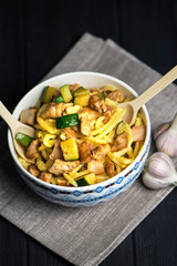 carbonara pasta with bacon, meat and zucchini in a bowl on a dark background