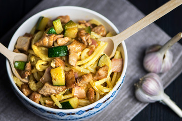 carbonara pasta with bacon, meat and zucchini in a bowl on a dark background