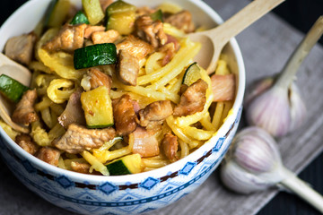 carbonara pasta with bacon, meat and zucchini in a bowl on a dark background