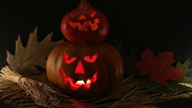Two halloween pumpkin lantern standing one on top of the other with burning candles surrounded by autumn leaves and spikelet against a black background 
