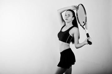 Fototapeta na wymiar Black and white portrait of beautiful young woman player in sports clothes holding tennis racket while standing against white background.