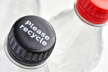 Plastic bottles and black and red bottle caps with please recycle message against a white background. Concept of plastic pollution.