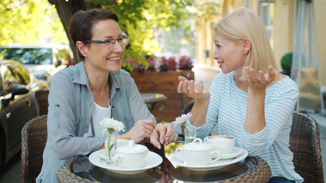 Cheerful adult women are laughing talking having fun relaxing in street cafe on summer day enjoying conversation and good company. People and joy concept.