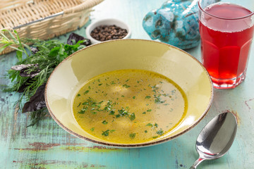 chicken broth with meatballs and herbs in bowl with glass of red drink on blue wooden table
