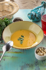 vegetable soup with cream and pumpkin and croutons and glass of red drink on blue wooden table