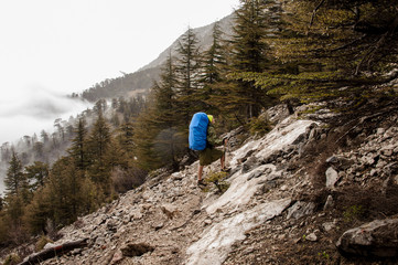 Girl in the raincoat walking up the rock with hiking backpack and sticks