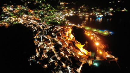 Aerial drone night shot of iconic illuminated medieval fortified castle overlooking the deep blue Aegean sea in Chora of Astypalaia, Dodecanese islands, Greece