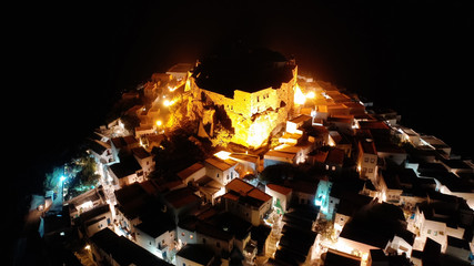 Aerial drone night shot of iconic illuminated medieval fortified castle overlooking the deep blue Aegean sea in Chora of Astypalaia, Dodecanese islands, Greece