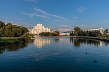 the river flows through it floating ducks on the background of a white building and green trees and above them the blue sky with Cirrus clouds