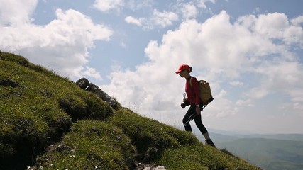 Girl photographer goes uphill on the background and the sky with clouds on a sunny day. Concept photo tours for landscape photographers. Mountain trekking