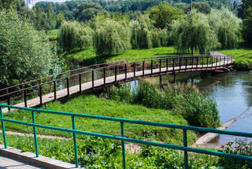 wooden bridge with iron handrails across the lake to the island where green willows grow