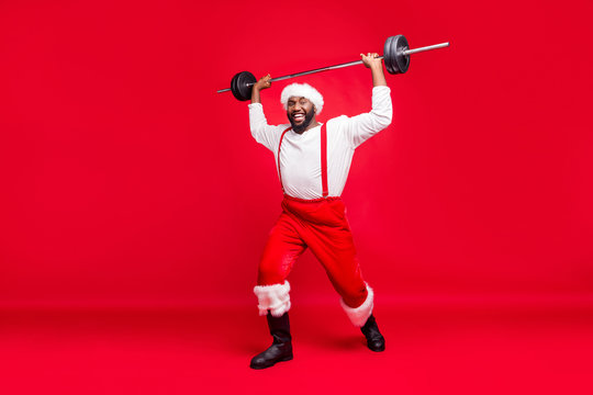 Full length photo of cheerful black santa claus in nicholas hat practice barbell wearing fashion white pullover pants trousers isolated over red background