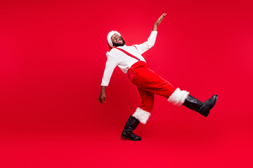 Fototapeta na wymiar Full size profile side photo of cheerful black santa claus going moving laughing wearing white pullover pants trousers isolated over red background