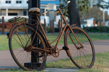 A rusty bicycle resting against a lamp post.