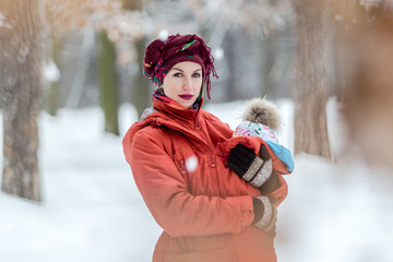 Mother carrying her baby girl wears red jacket and sling.