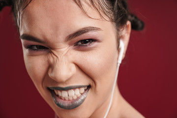 Image closeup of sassy punk girl with bizarre hairstyle and dark lipstick wrinkling her nose while using earphones