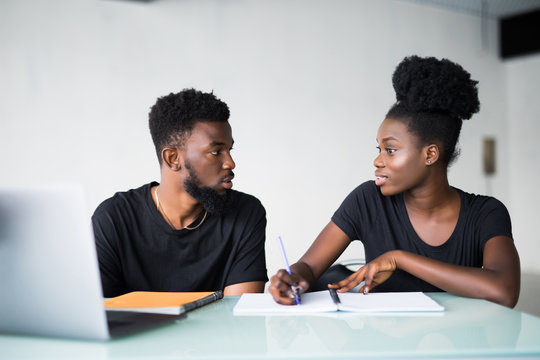 Happy African American couple of enterpreneurs develop new business strategy on portable laptop computer, use mobile phones for surfing information in internet, sit together in office room
