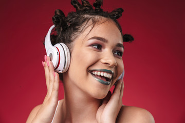 Fototapeta premium Image of extreme punk girl with bizarre hairstyle and dark lipstick smiling while listening to music with headphones