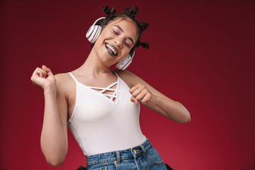 Fototapeta premium Image of pleased punk girl with bizarre hairstyle singing and dancing while listening to music with headphones