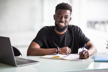 Young African man looking at camera with laptop in modern office