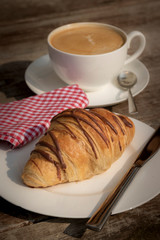 Coffee cup and fresh baked croissants on wooden background.