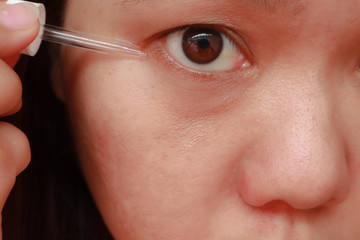 Asian woman applying anti-ageing moisturizing serum to under eye area.