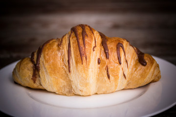 Coffee cup and fresh baked croissants on wooden background.