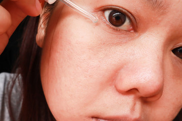 Obraz premium Asian woman applying anti-ageing moisturizing serum to under eye area.