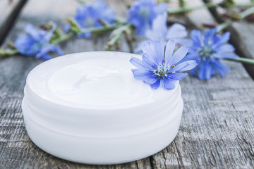 Fototapeta na wymiar Face cream with the addition of chicory in a white jar near the flowers of chicory on an old wooden table. Health concept.