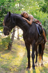 Fototapeta premium Young woman in a bright colorful dress riding a black horse